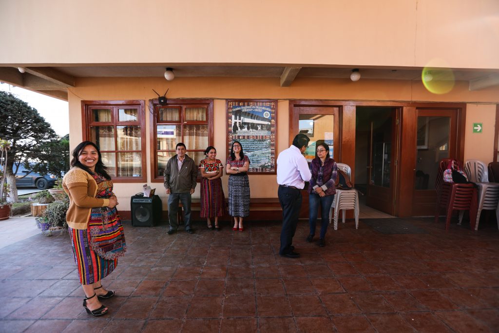 Leaders of the regional community association of farmers (CDRO) stand on a covered tiled patio with representatives from Guatemala's national meteorological service (INSIVUMEH). The women wear traditional Indigenous dress, with brightly striped skirts. 