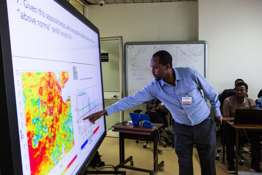 An Ethiopian workshop participant in a blue collared shirt with a ID tag clipped to his shirt points to a large screen with a weather map and accompanying graph. Other seated participants look on from the background.

A participant shares the result of his small group's work on an exercise during a training held at the National Meteorological Agency in Addis Ababa in October of 2018. Photographer Elisabeth Gawthrop, ACToday/IRI.