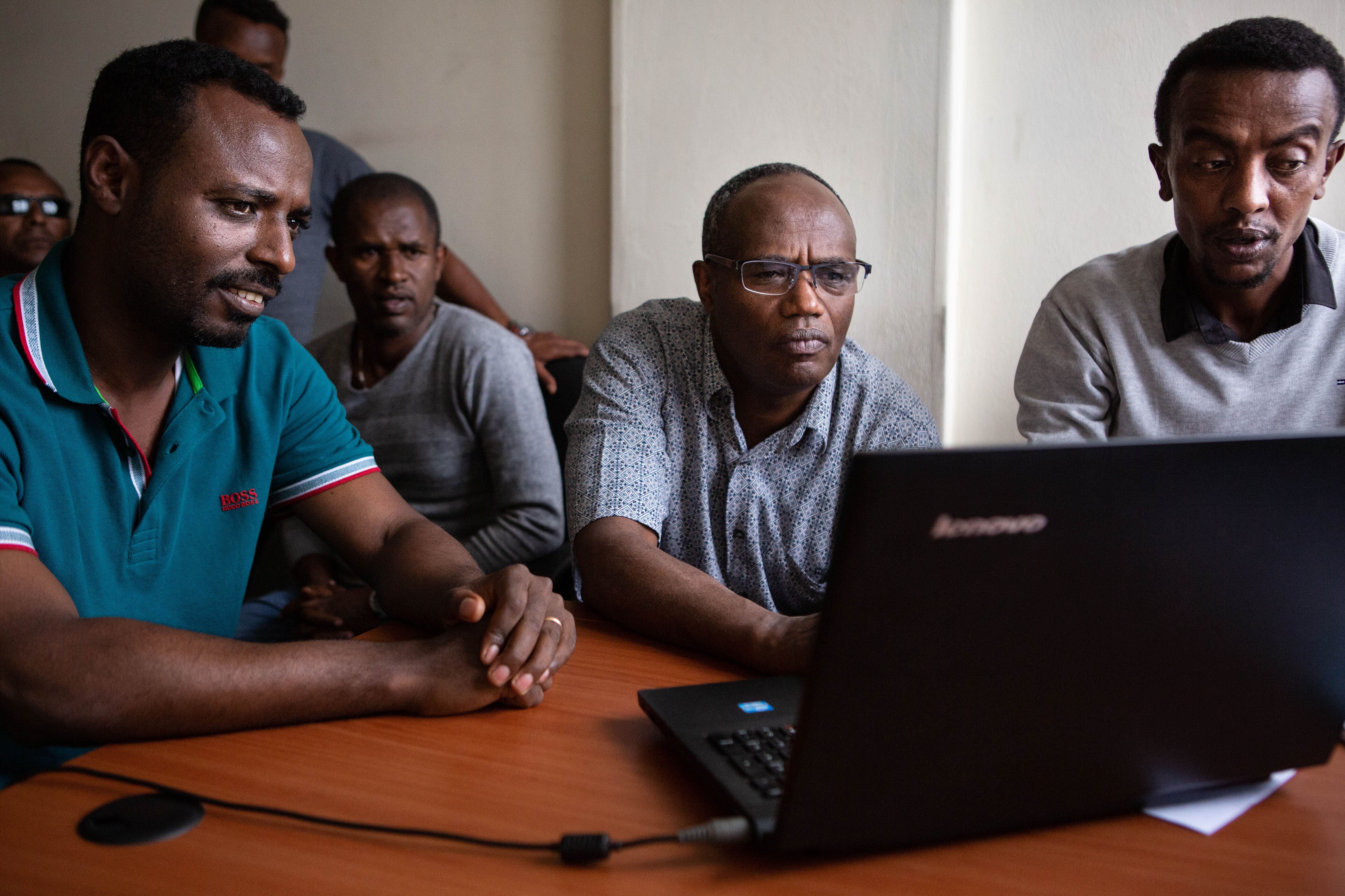 Tufa Dinku, the country lead for ACToday Ethiopia, demonstrates the maprooms with a team from the National Meteorological Agency. Dr. Dinku squints at a laptop whose screen faces away from the camera and his hand hovers over the scrollpad. On either side of him are members of the Ethiopian National Meteorological Agency who look on with interest at the screen.